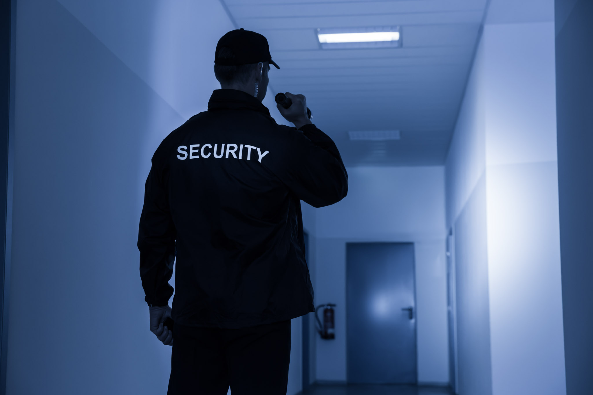 Ein Security Mann in einer schwarzen Jacke leuchtet im Dunkeln den Flur aus.